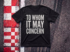 To Whom it May Concern F1 t-shirt in Black, flat lay on a race track kerb