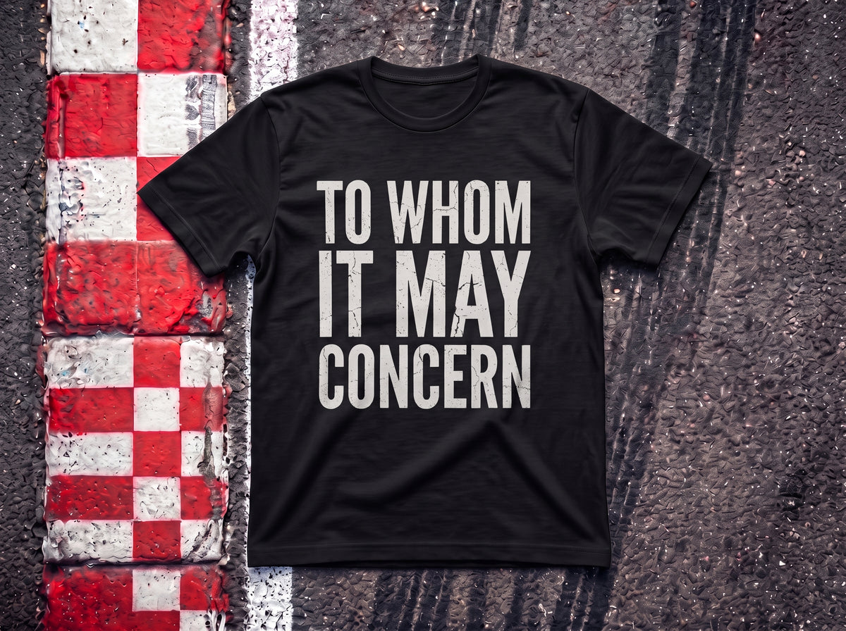 To Whom it May Concern F1 t-shirt in Black, flat lay on a race track kerb